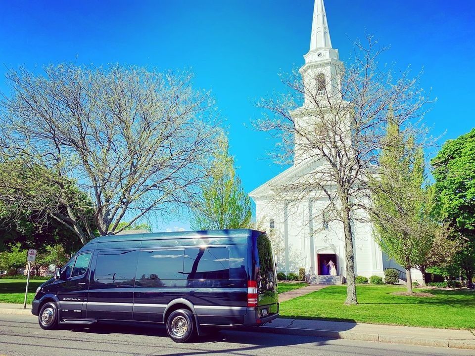 Dark van parked in front of a white church with a steeple on a sunny day.
