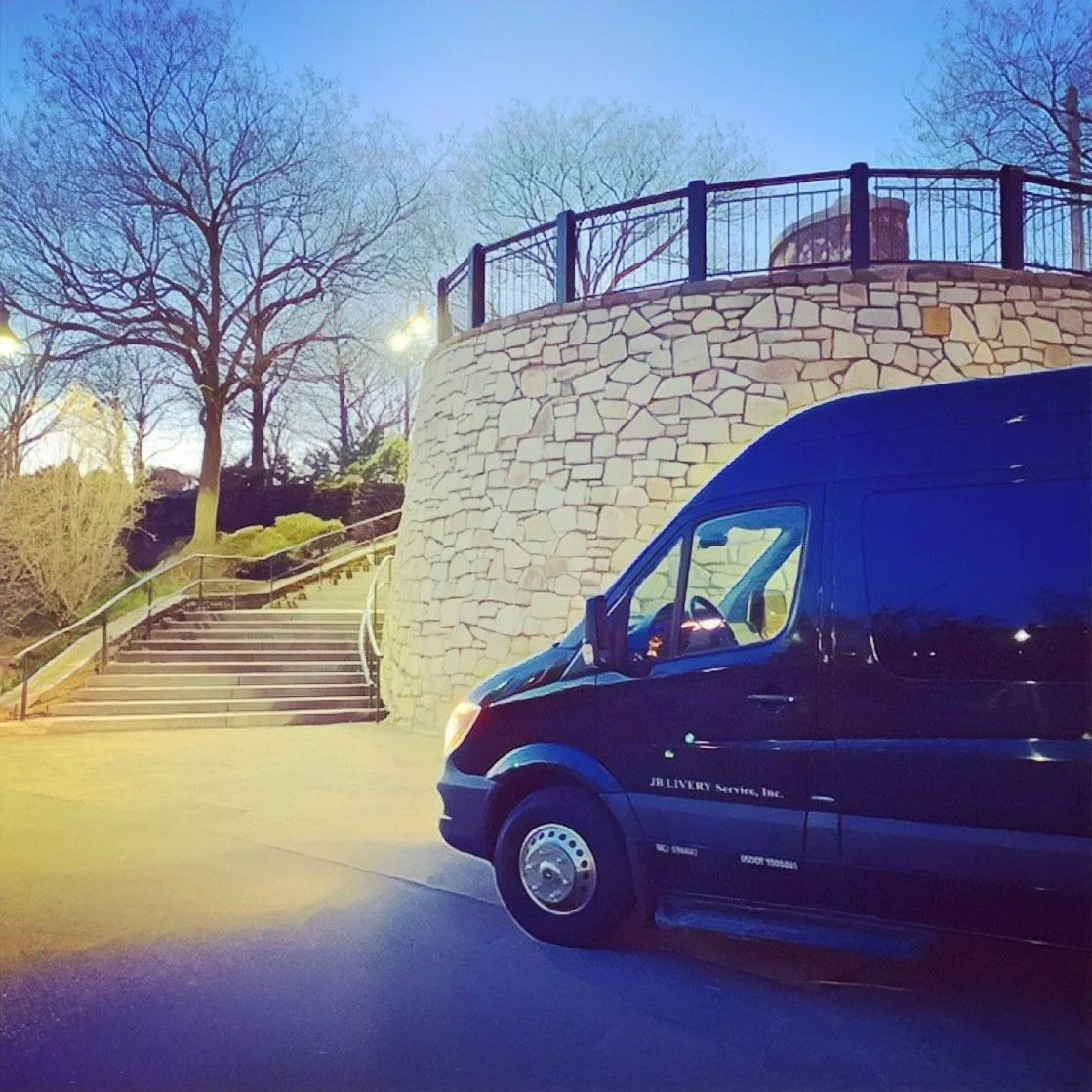 Black passenger van parked near stone wall and steps leading up to a viewing platform.