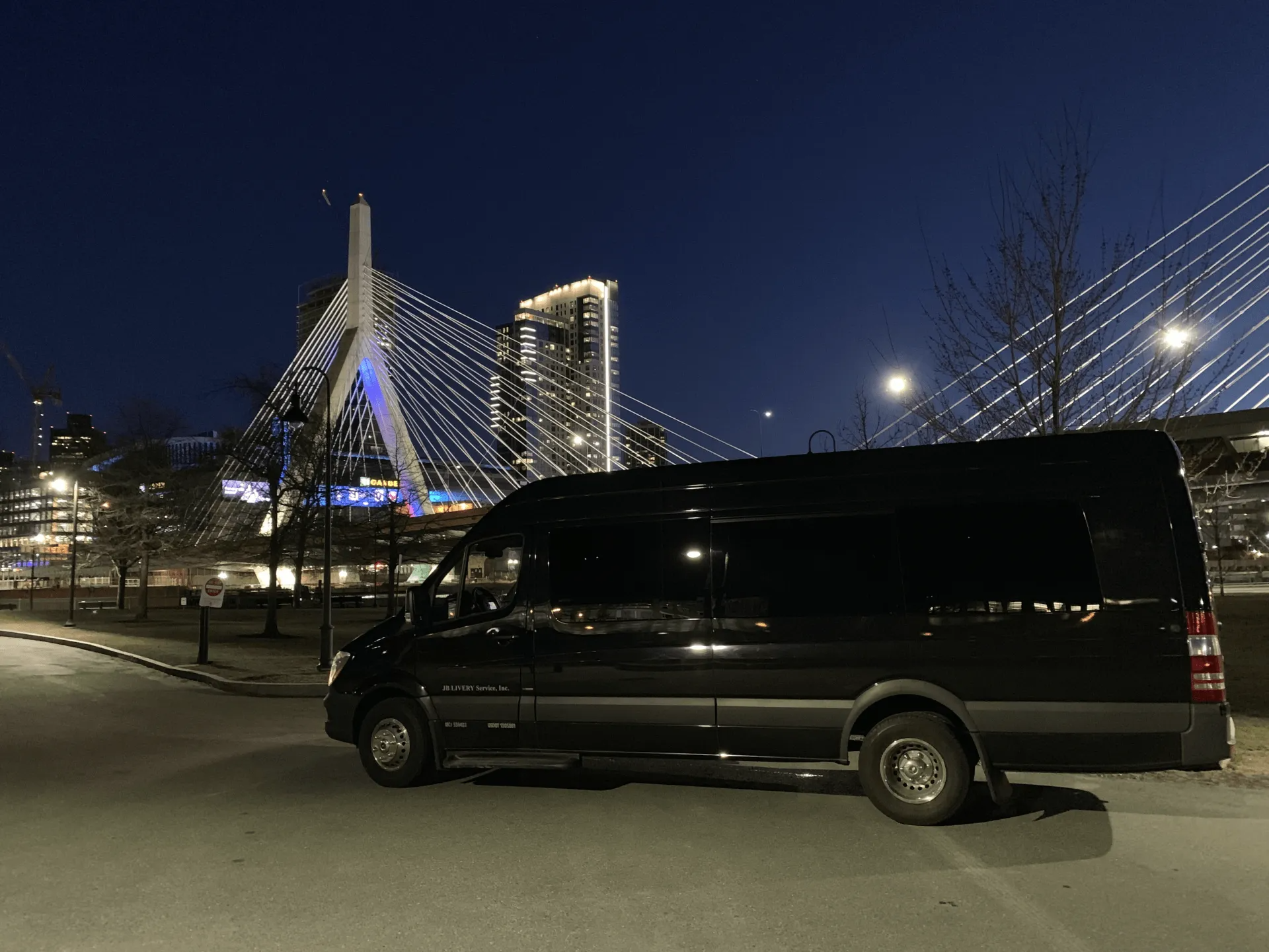 Black van parked near a bridge with city lights at night.