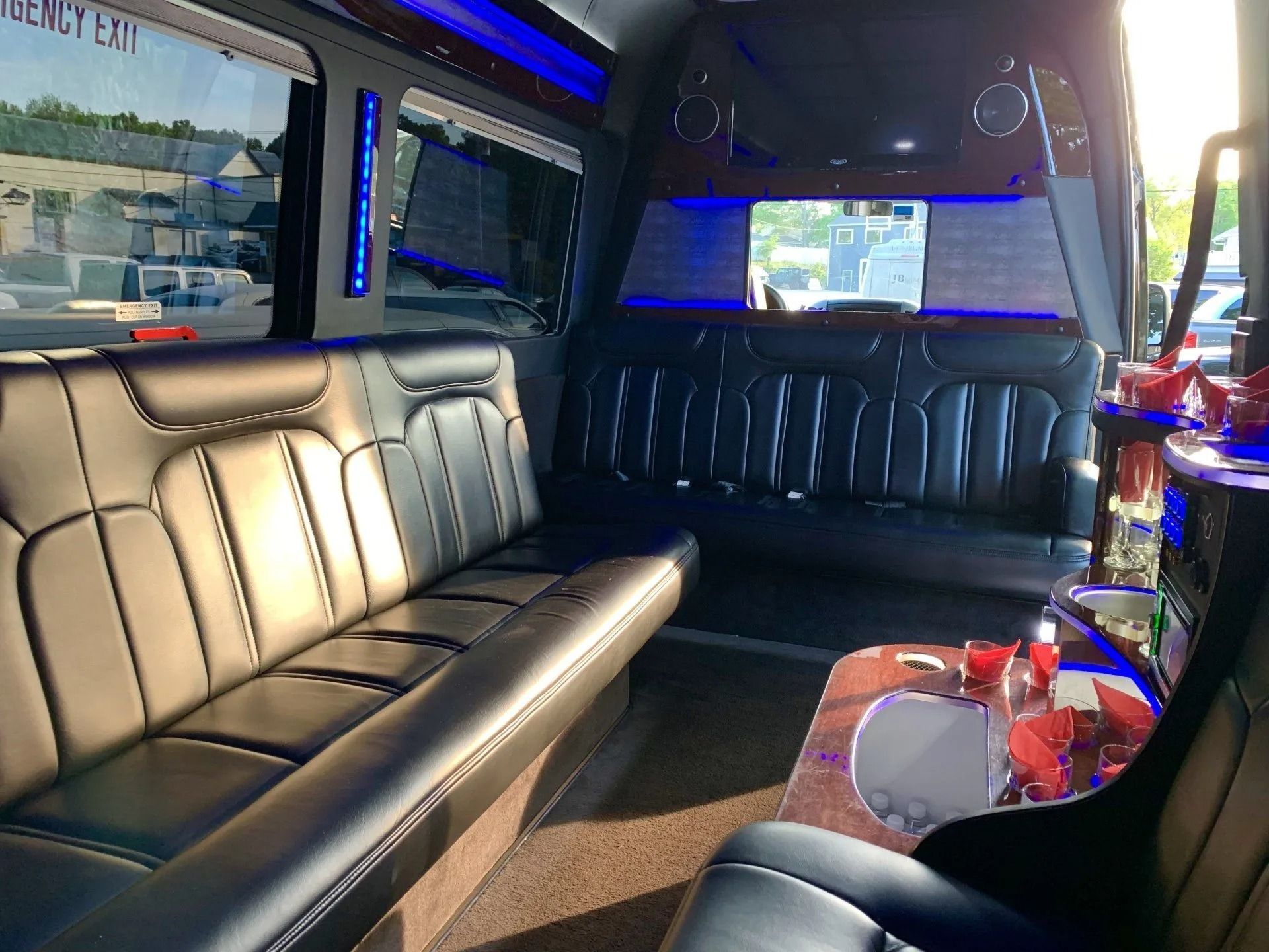 Interior of a black luxury van with leather seating, a bar area, and blue accent lighting.