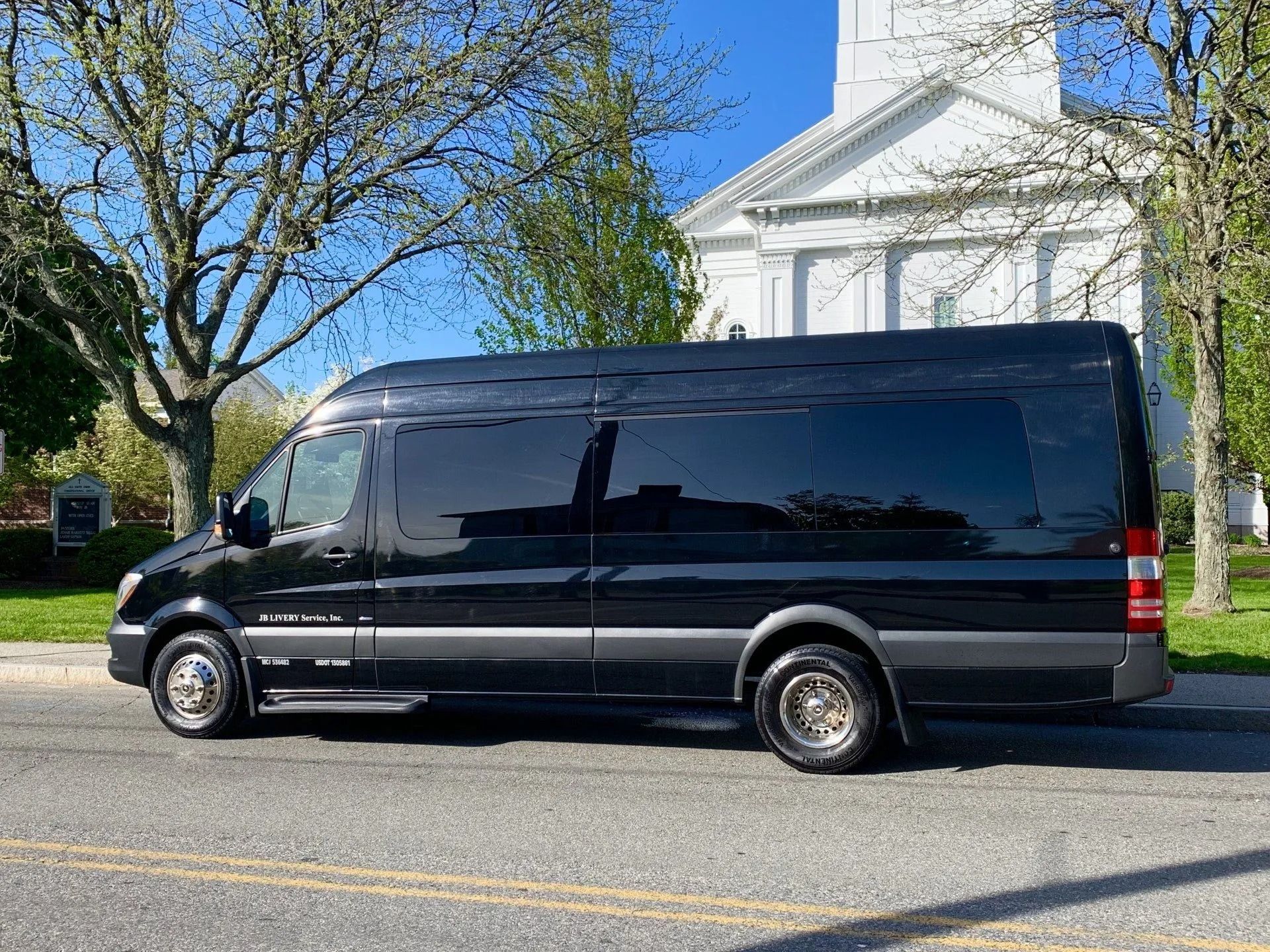 Black passenger van parked on a street in front of a white church.