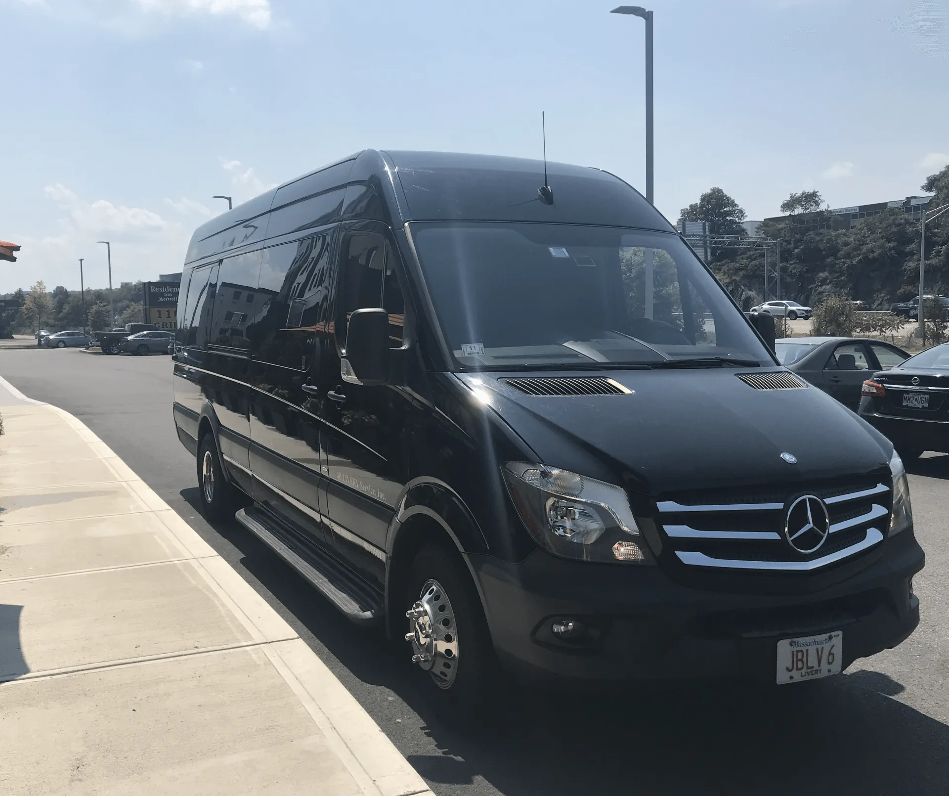 Black Mercedes-Benz Sprinter van parked on a paved street. Sunny day, other vehicles in the background.