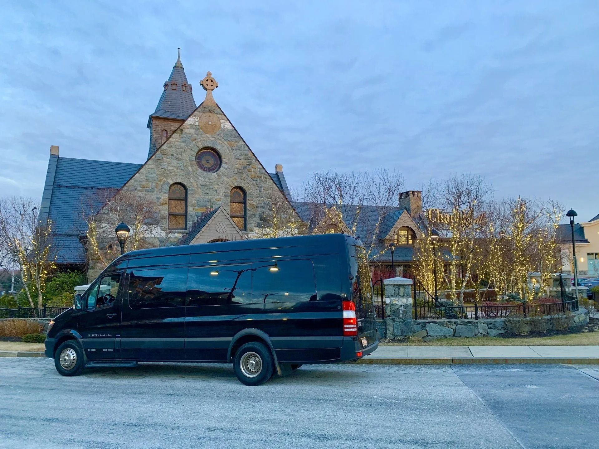 Black van parked in front of a stone church with a steeple, under a cloudy sky.