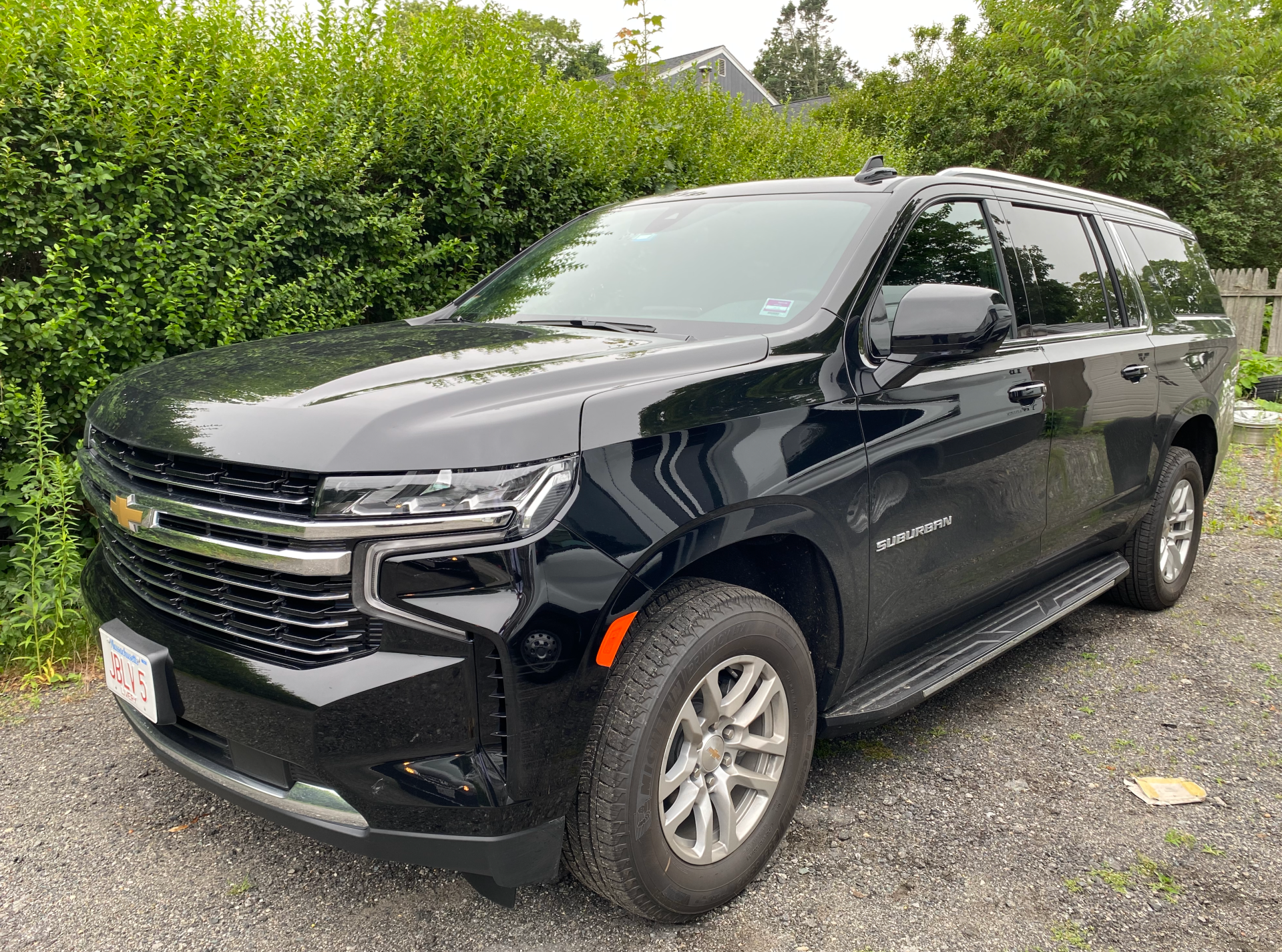 Black Chevrolet Suburban SUV parked on gravel, in front of a green hedge.