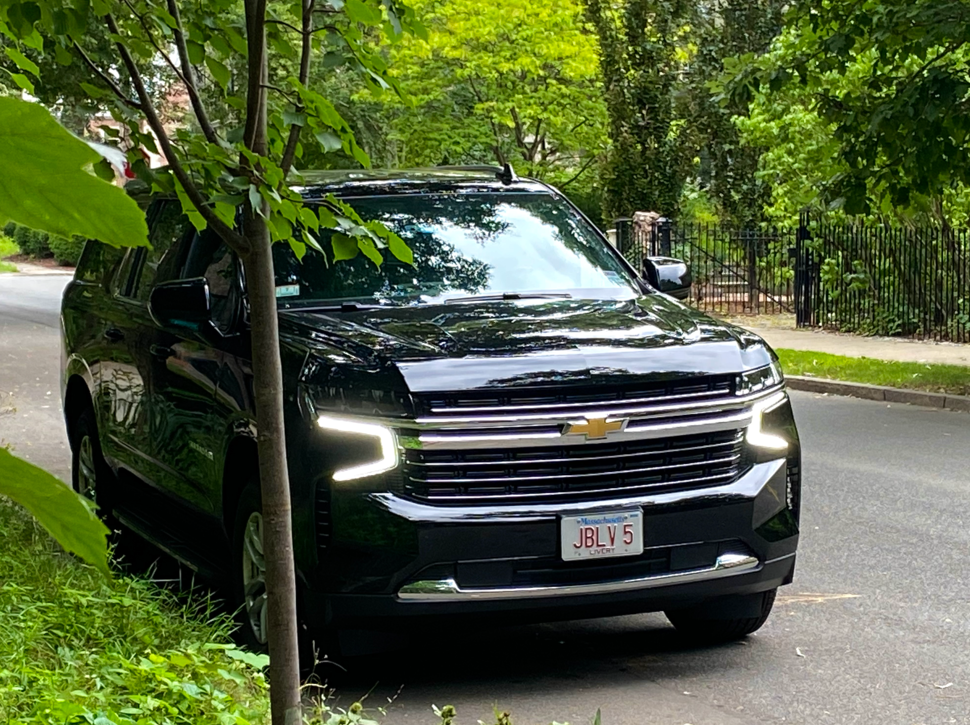 Black Chevy SUV parked on a tree-lined street; Massachusetts license plate; sunny day.