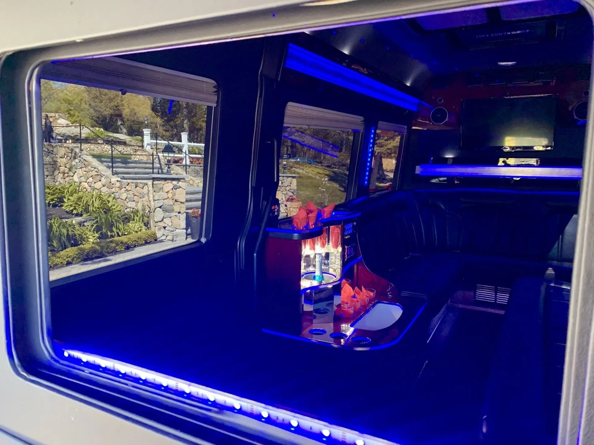 Interior of a limo with blue lights, a bar, and a view of a landscape outside.