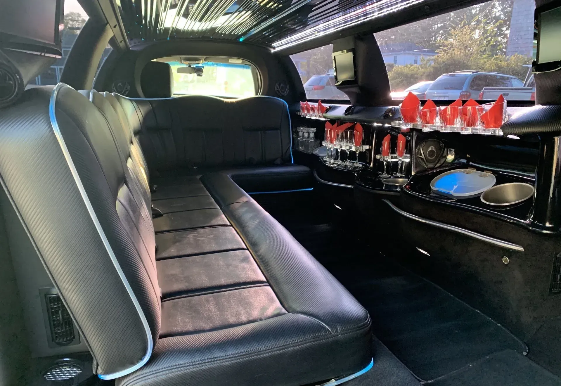 Interior of a black limousine with black leather seating, bar, and decorative lights.