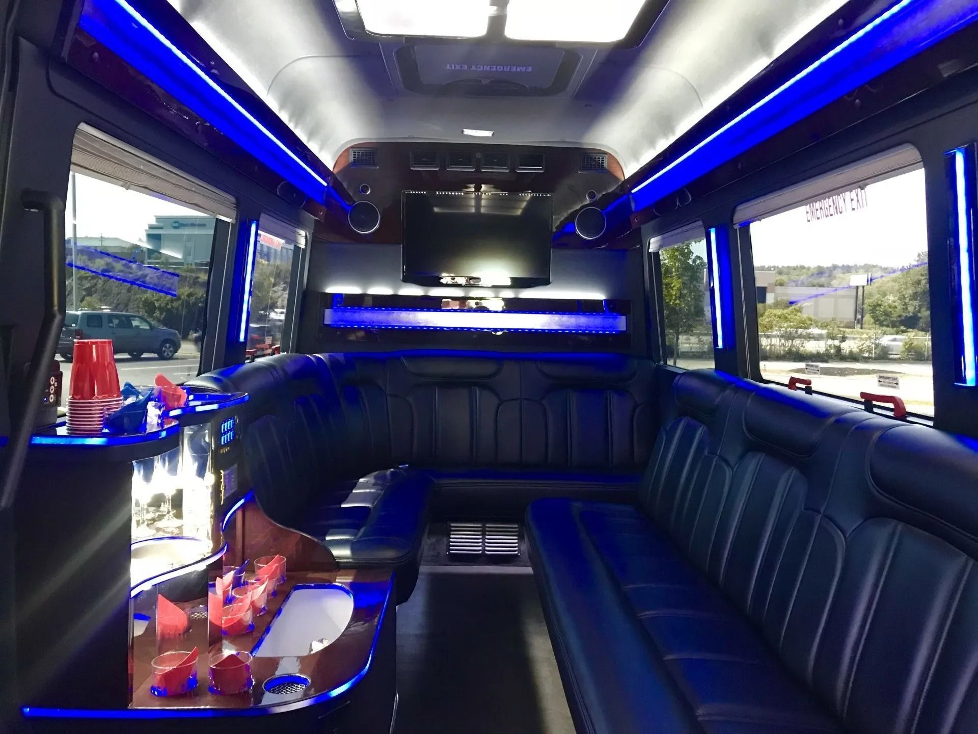 Interior of a party bus with black leather seating, blue lights, bar area.