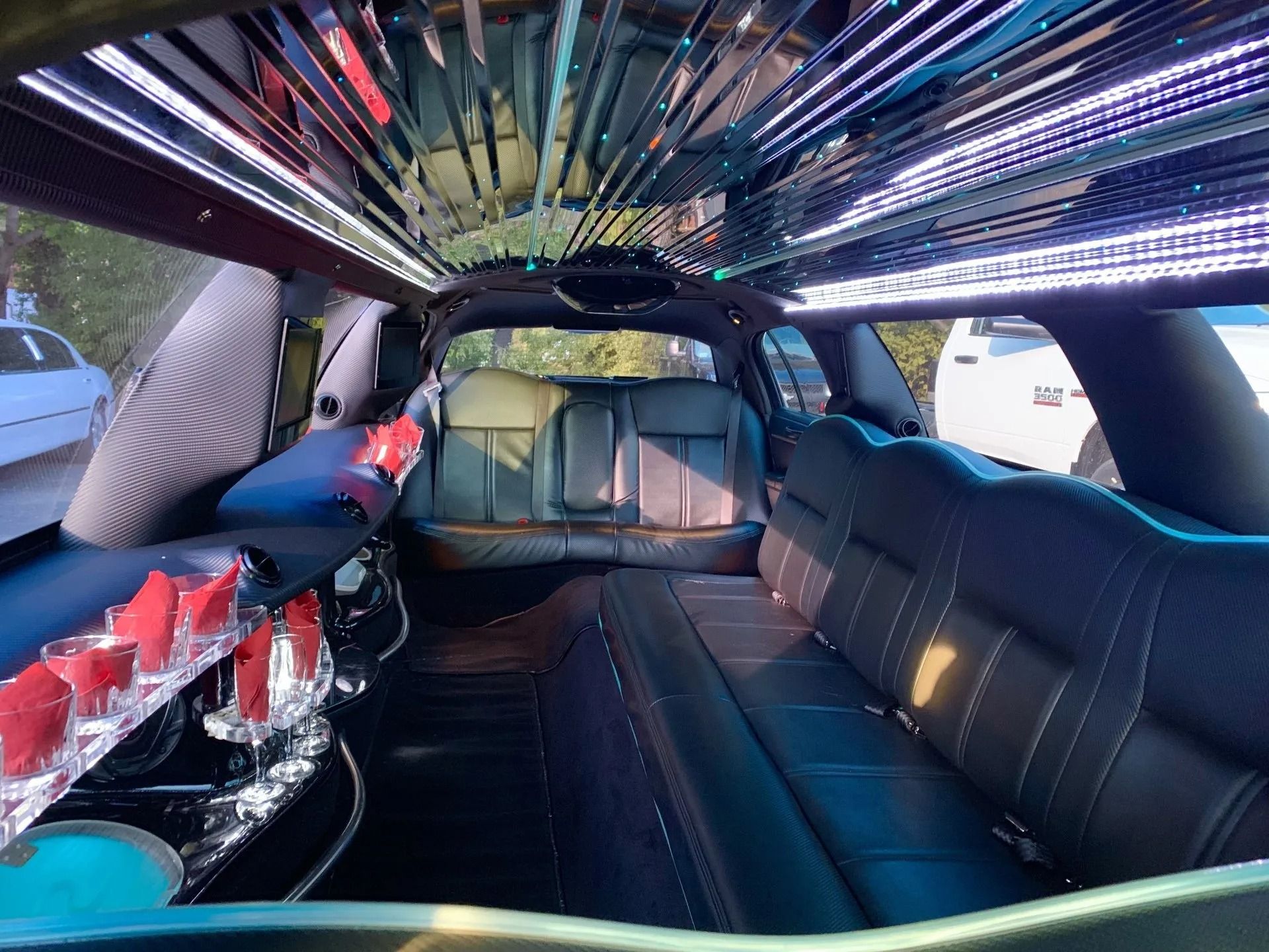 Interior of a limousine with black leather seating, neon lights, and mirrored ceiling.
