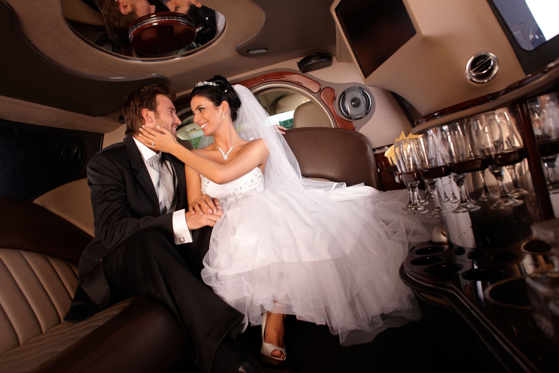 Bride and groom in a limousine, smiling at each other. She wears a white dress, he wears a suit.