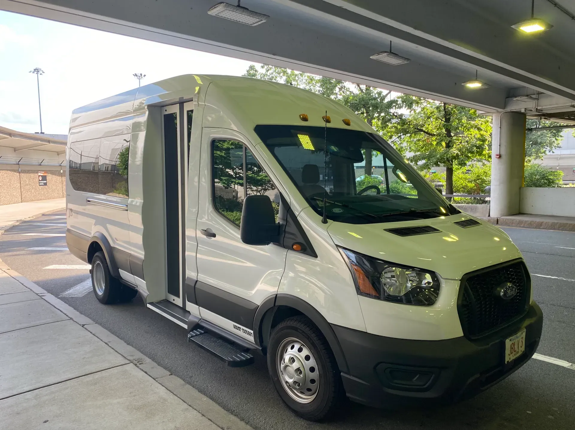 White passenger van with accessible side door and ramp parked under a building overhang.