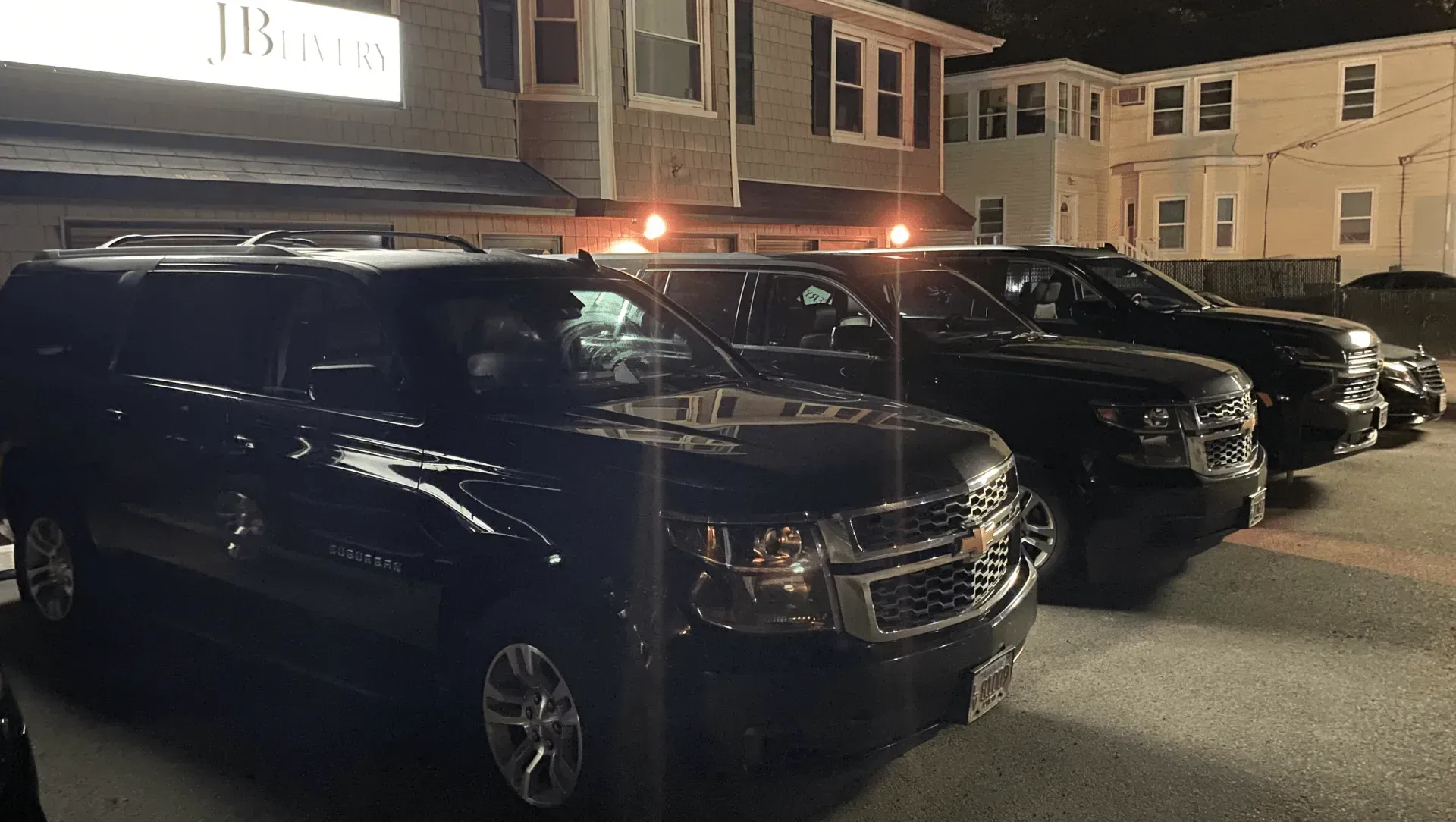 Black hearses and limousines parked outdoors, under trees, in a sunny area.