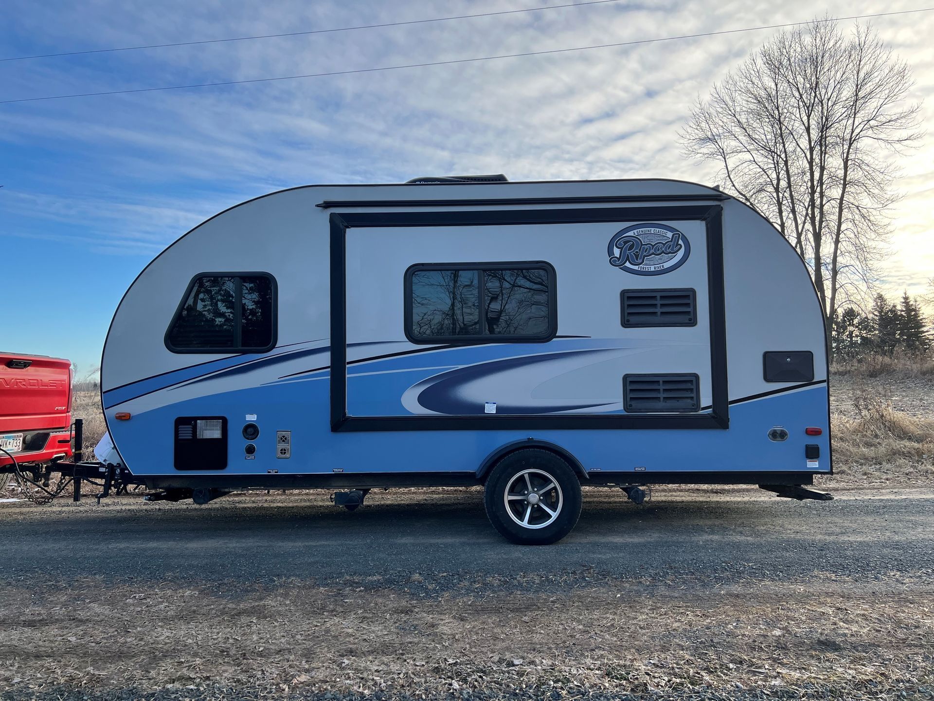 A small blue and white RV trailer is parked in a gravel lot.