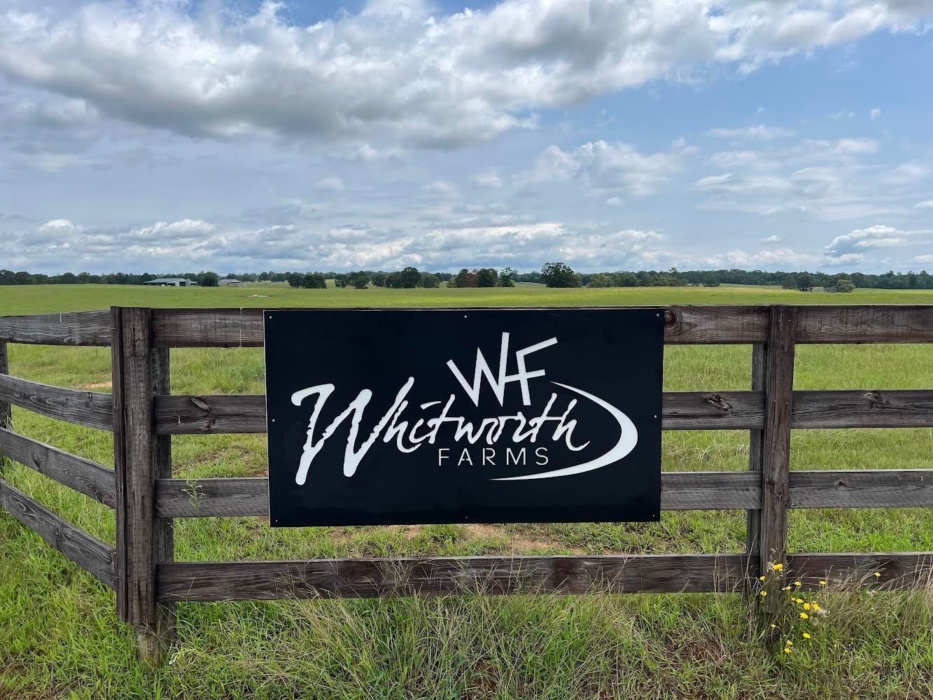 a black sign is hanging on a wooden fence in front of a field