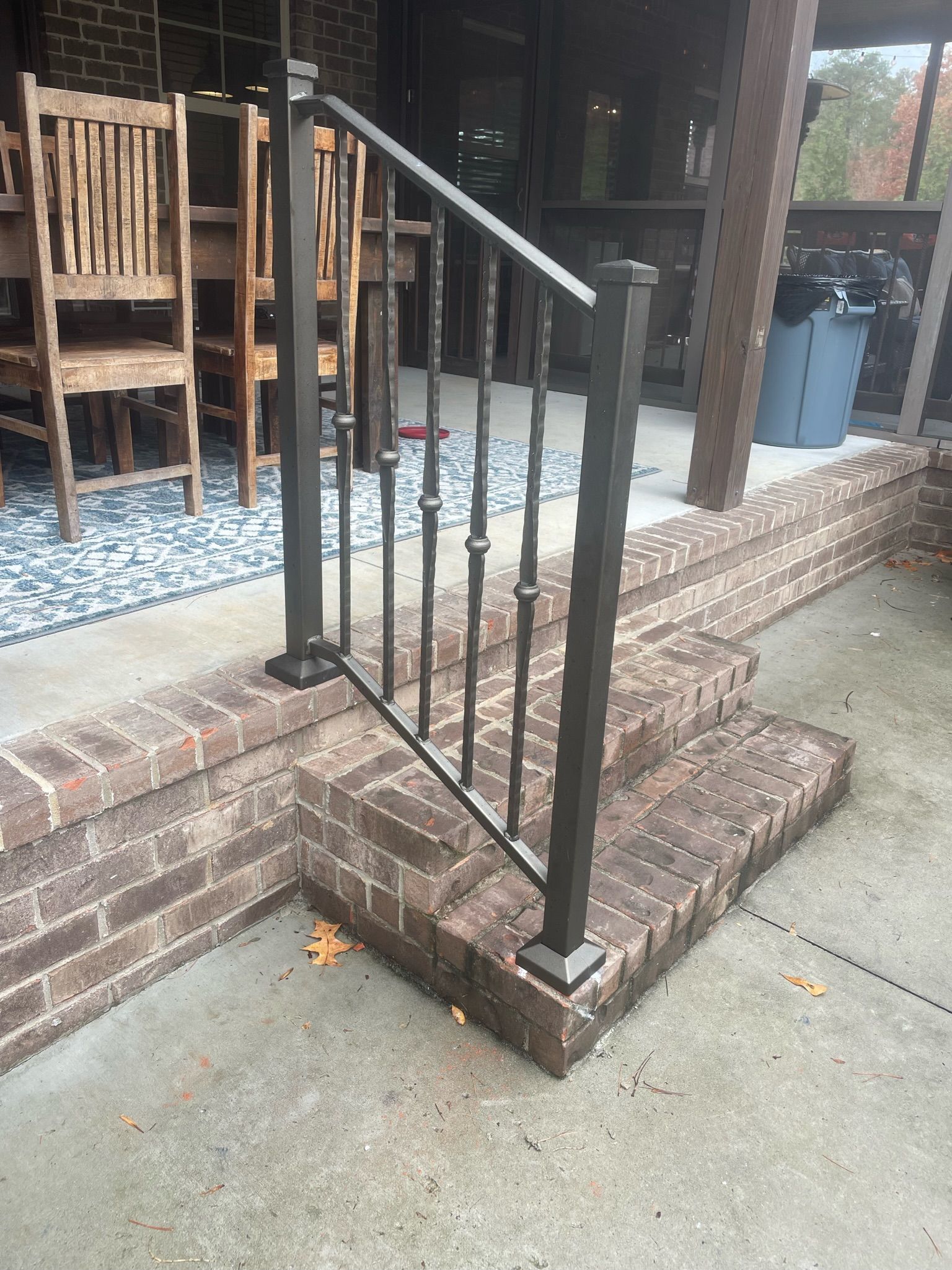 a wrought iron railing on a brick porch next to a table and chairs