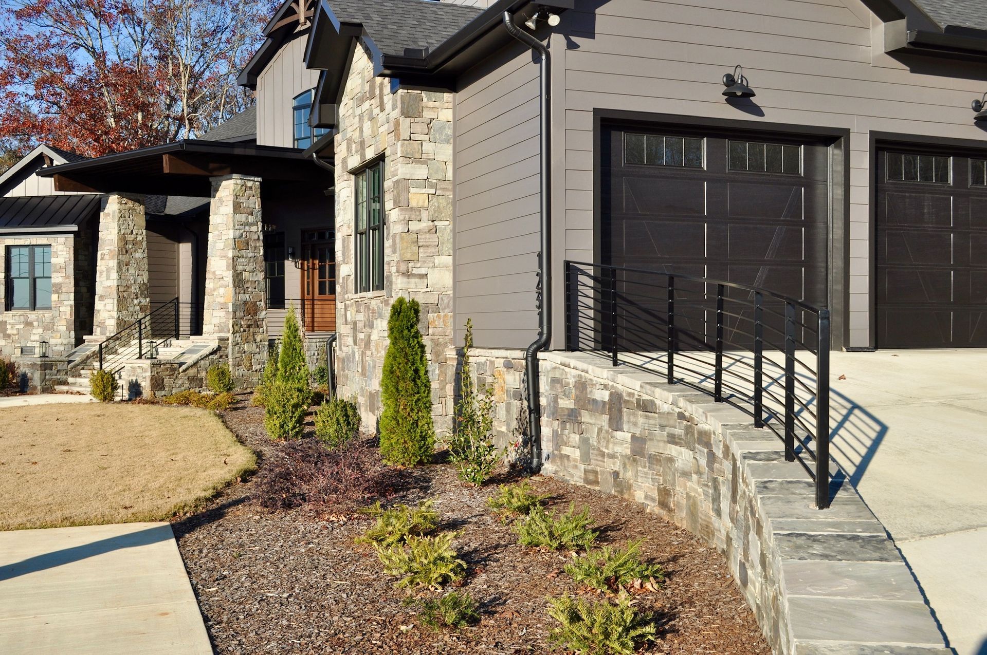 a house with two garage doors and a stone wall in front of it