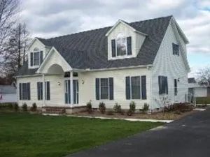 White two-story house with dark gray roof, black shutters, and green lawn.