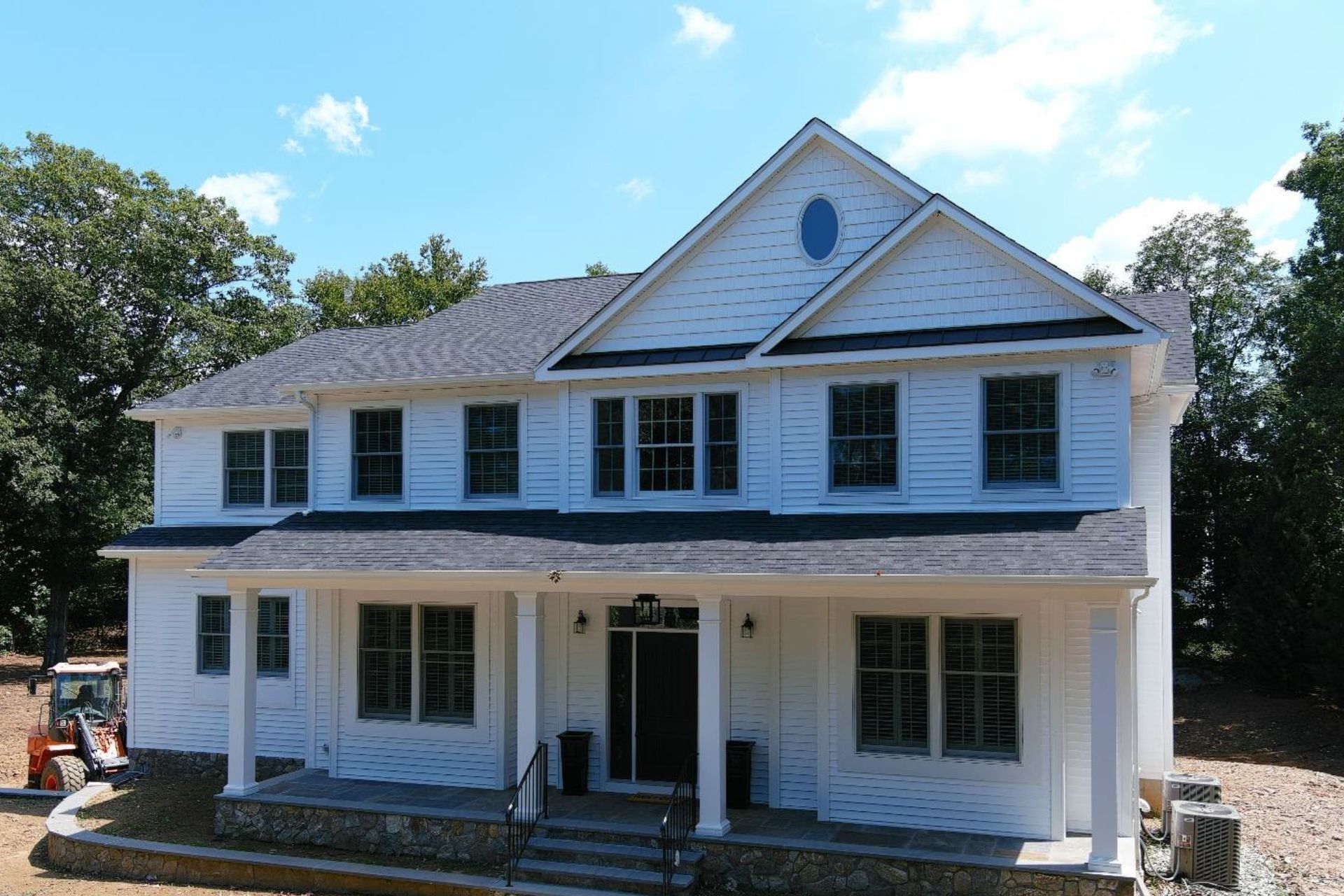 Two-story white house with a dark roof and large windows under a blue sky, construction in progress.