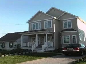 Two-story house with a porch and a car in the driveway on a sunny day.