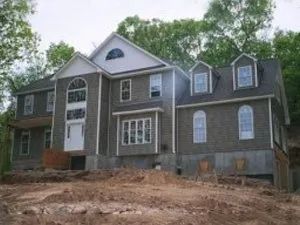 House under construction with gray siding, white trim, and a dirt yard.