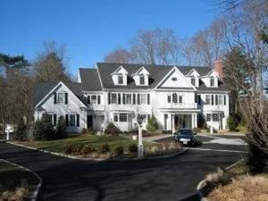 White two-story house with black shutters and a black asphalt driveway on a sunny day.