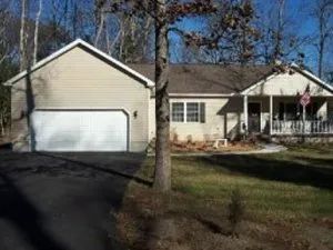 Beige ranch-style house with attached garage, porch, and American flag on a grassy lawn.