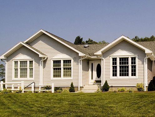 A light grey house with white trim, windows, and front door, set on green grass.
