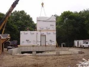Crane lifting a modular building unit to be stacked on a pre-built foundation. Construction site.