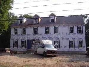 House under construction with windows and dormers, wrapped in Tyvek. White van parked in front.