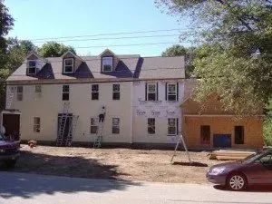 Multi-story building under construction; workers on ladders, side of building sheathed in paper.