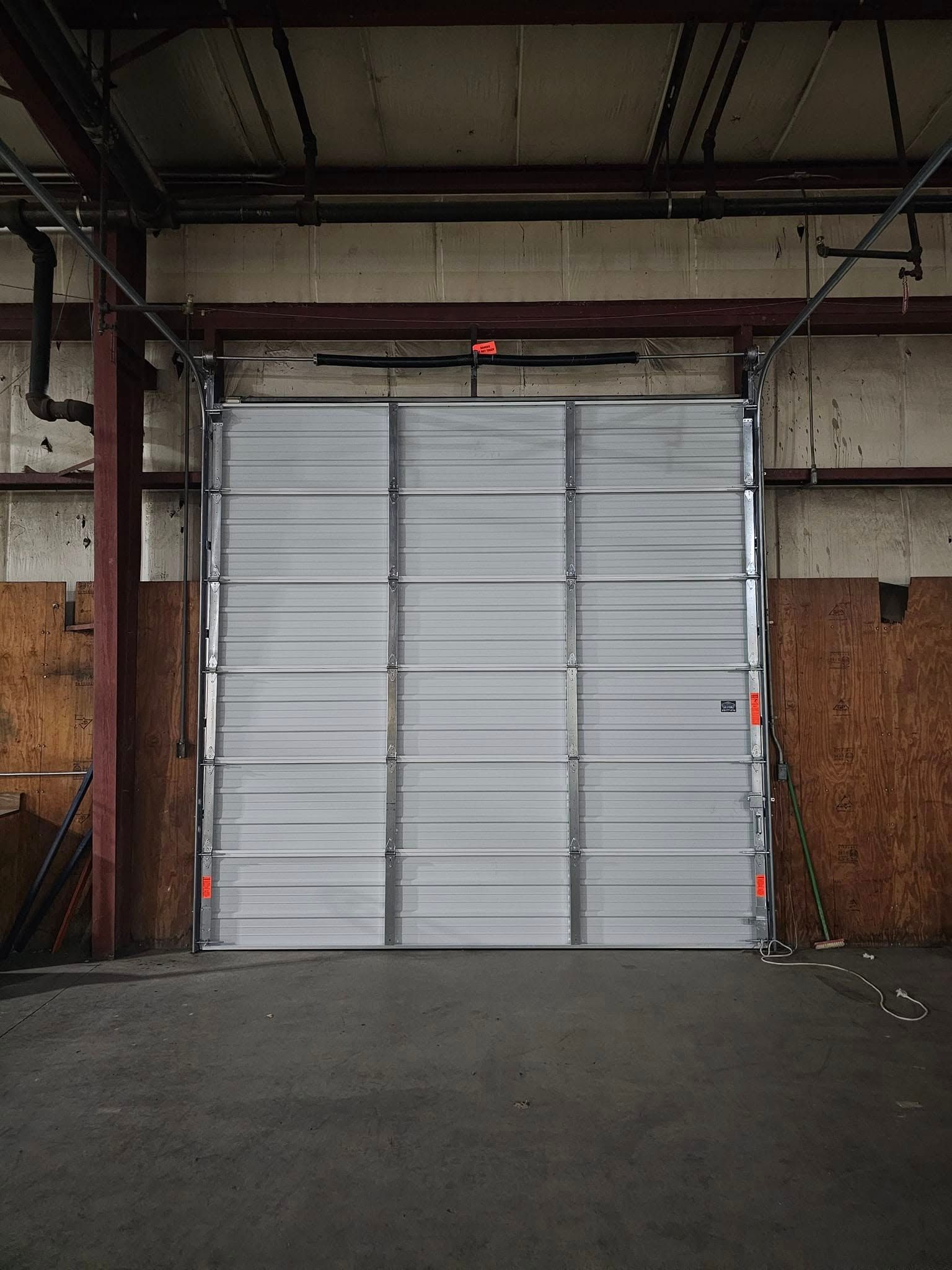 A large white garage door is open in an empty warehouse.