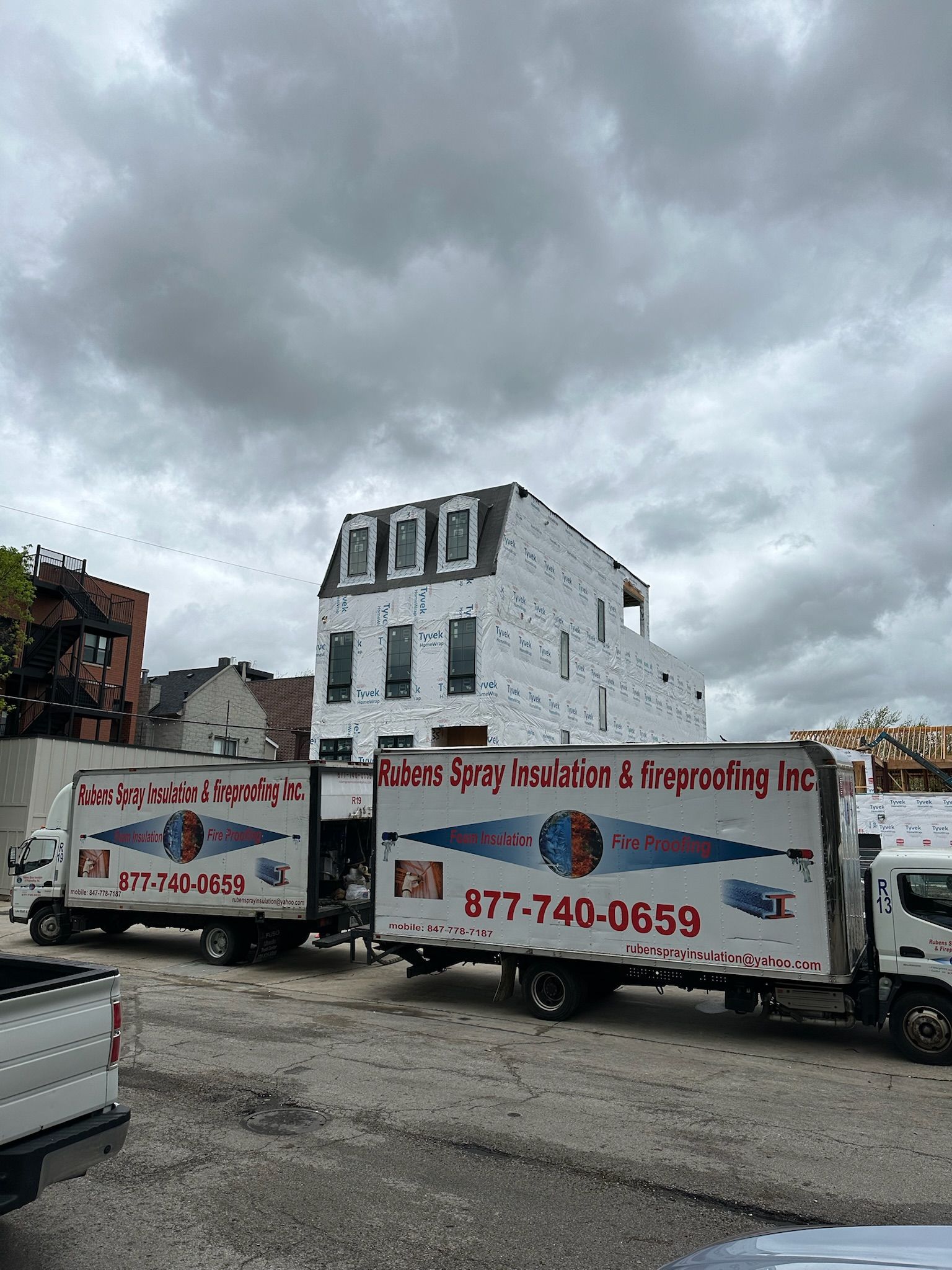 Two moving trucks are parked in front of a building under construction.