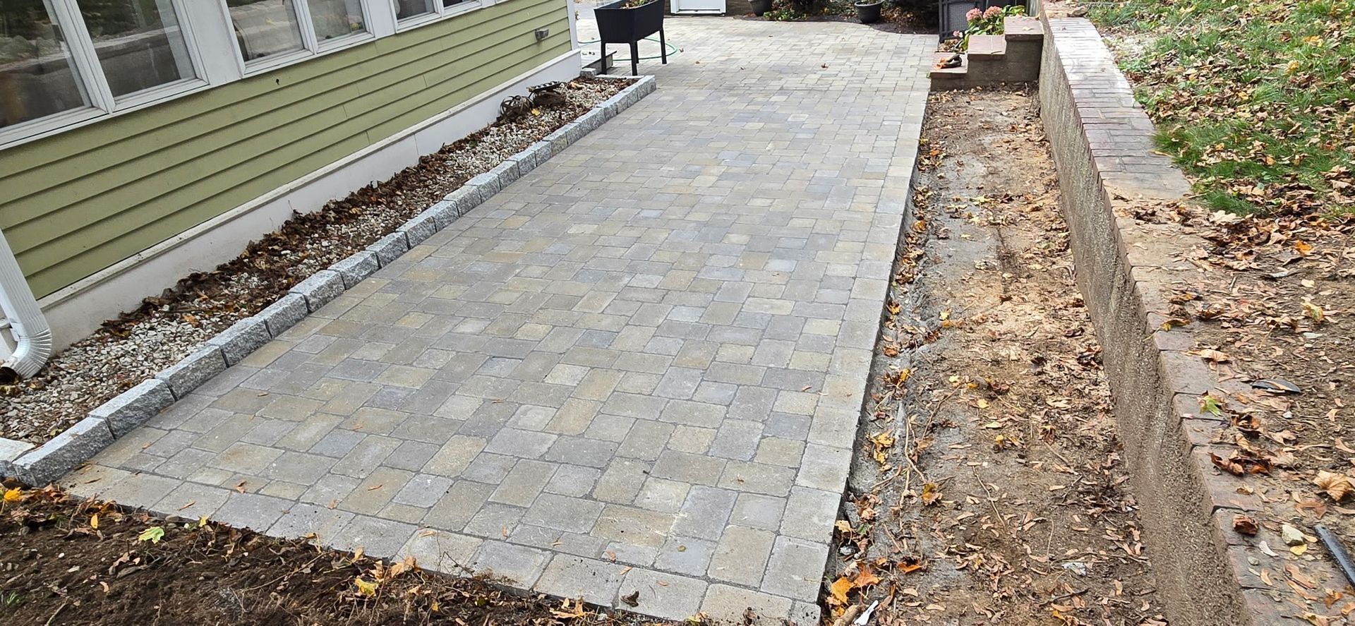 A paved patio next to a house with a gravel border. A retaining wall lines the edge of the patio.