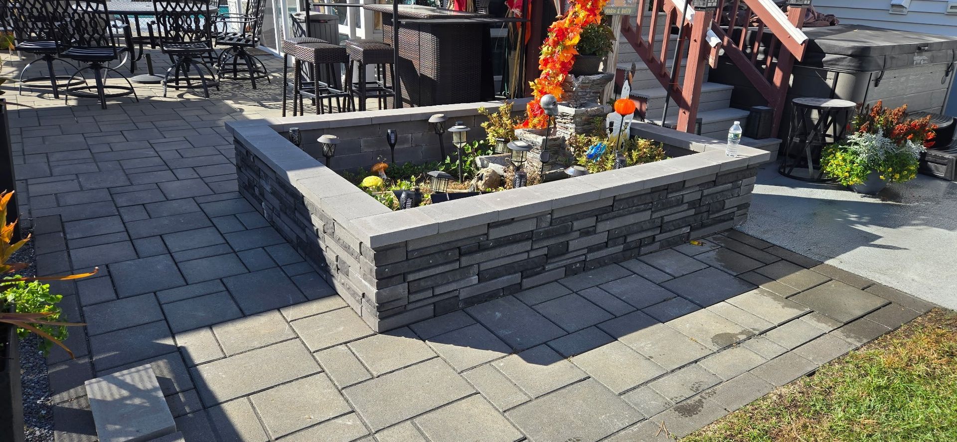 A paved outdoor patio with a stone planter filled with flowers and decorations.