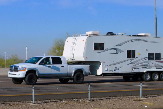 White pickup truck towing a large white and gray travel trailer on a sunny road.