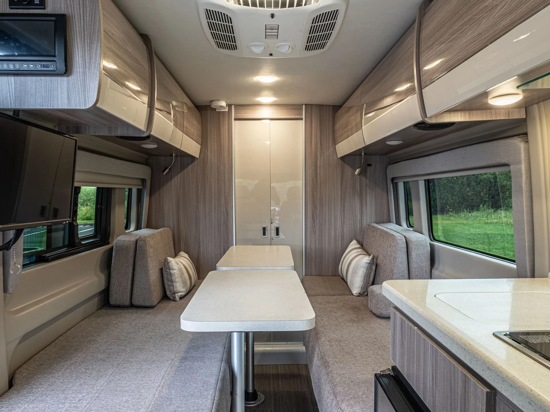 Interior of a camper van with seating, tables, overhead cabinets, and a kitchen counter.