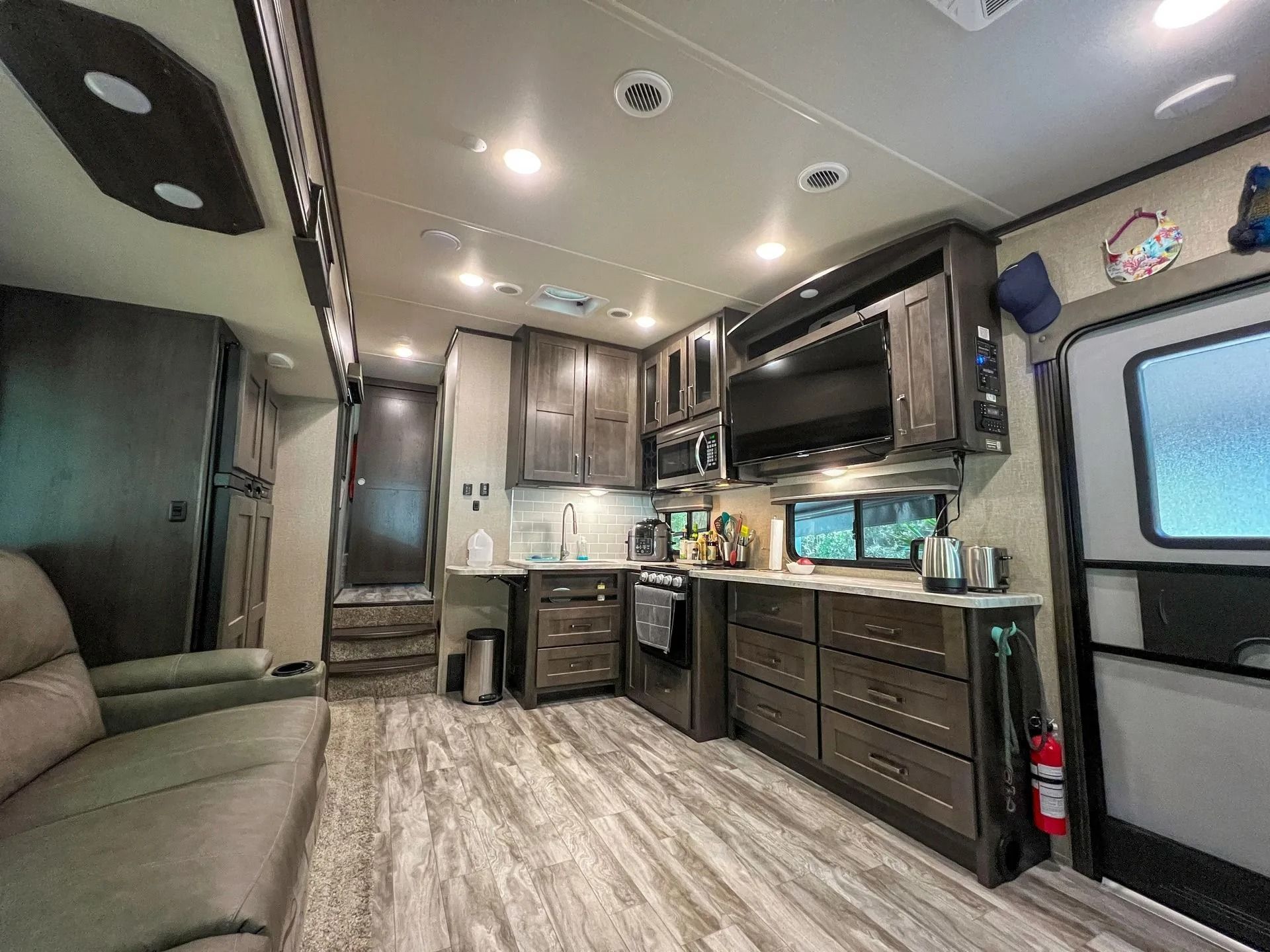 RV interior, featuring a kitchen with dark cabinetry, appliances, and a couch.