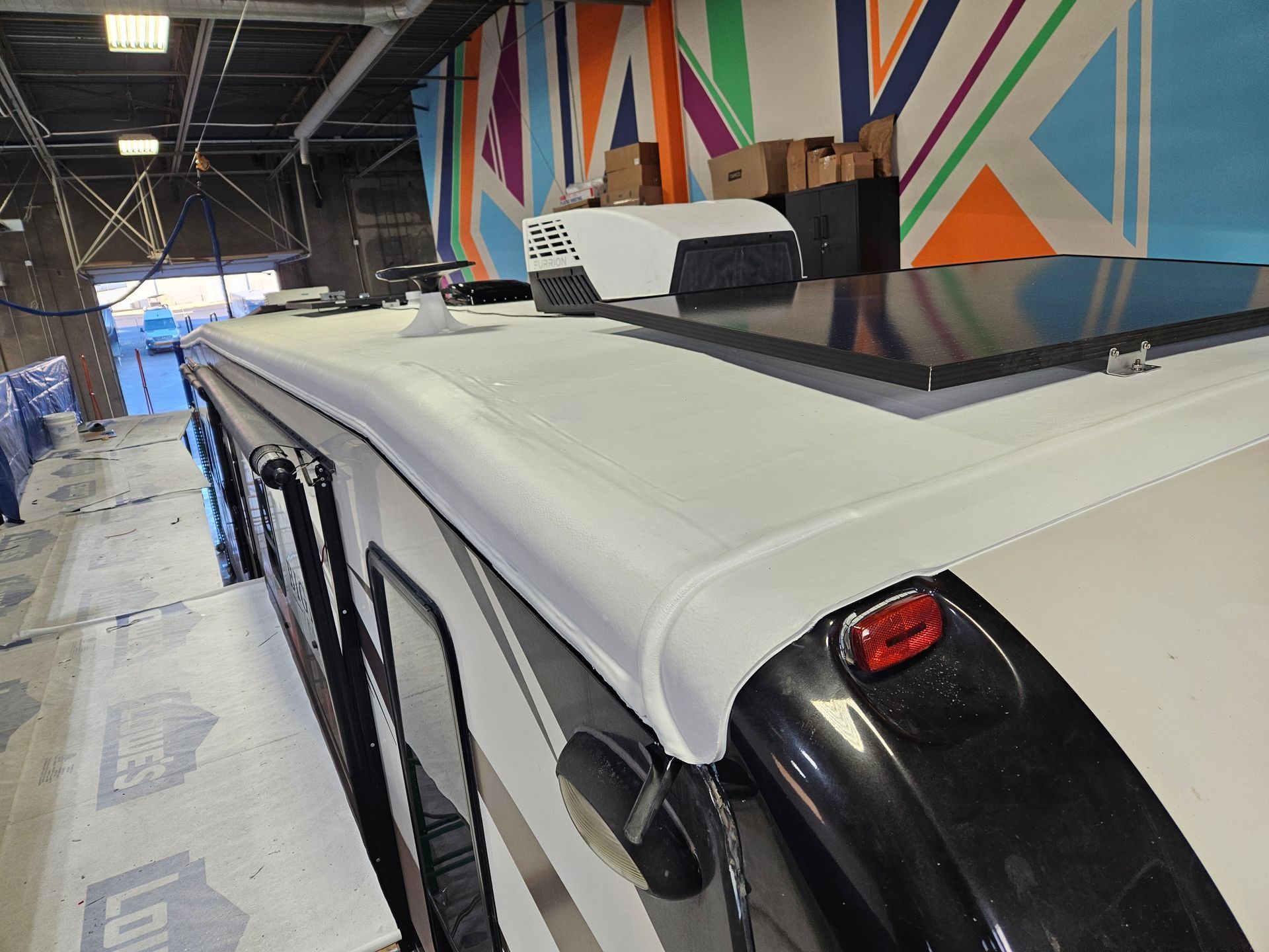 RV camper with awning extended in a wooded campsite, red chairs on a rug.