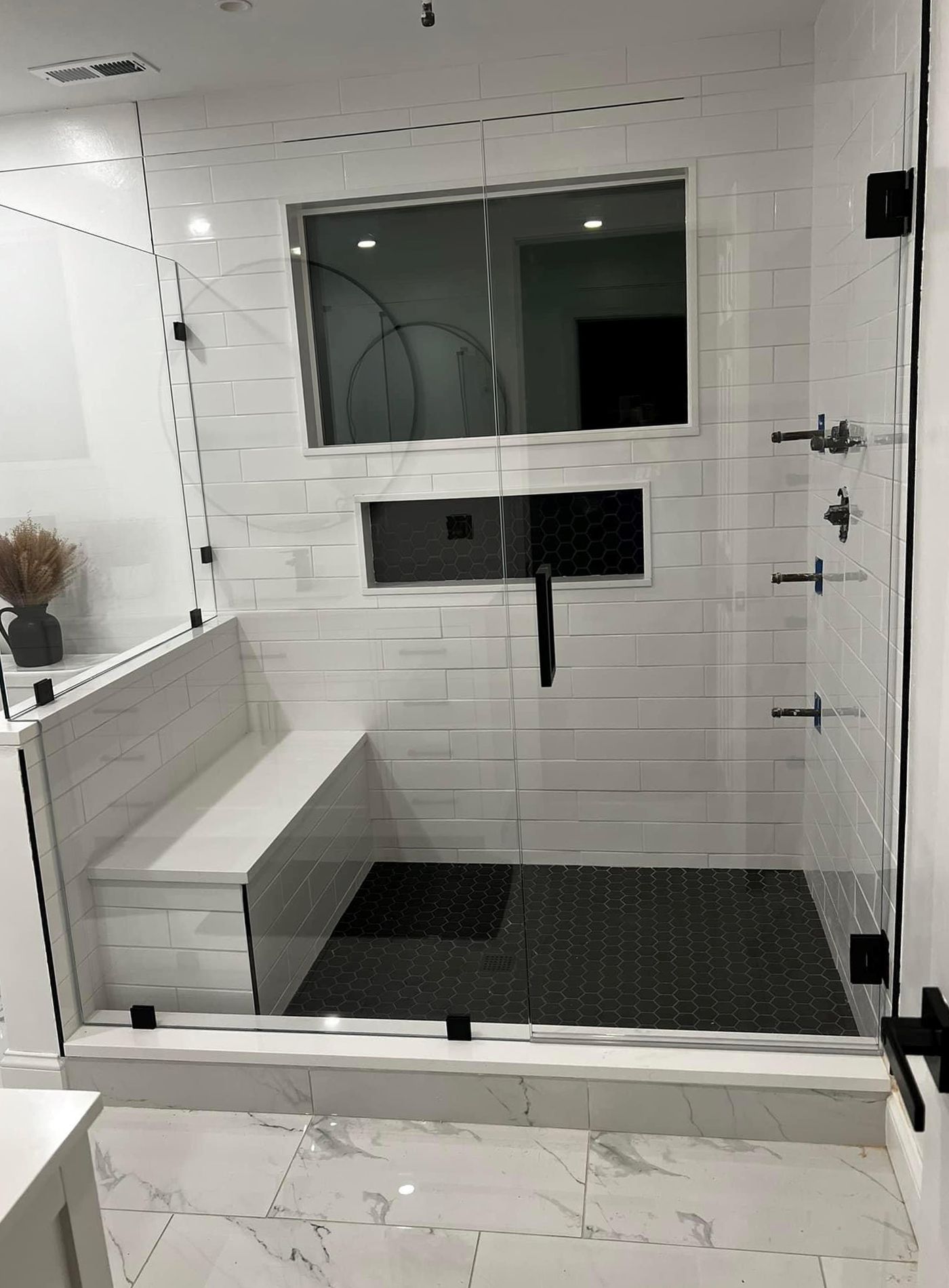 A bathroom with a walk in shower with a bench and a window.