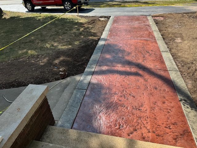 Red stamped concrete walkway leading from stairs to street, bordered by concrete.