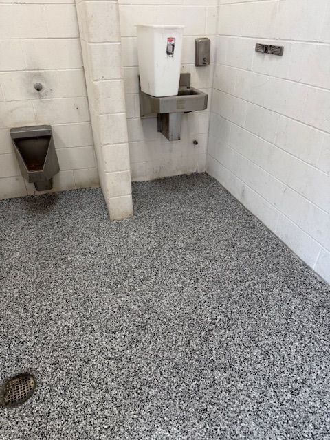 Public restroom with speckled gray floor, urinal, sink, and white walls.