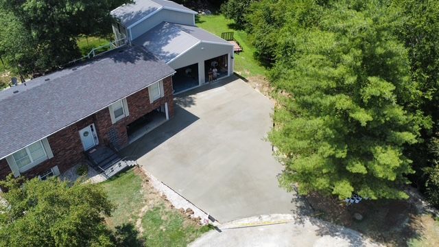Aerial view of a house with a newly poured concrete driveway and attached garage, surrounded by trees.