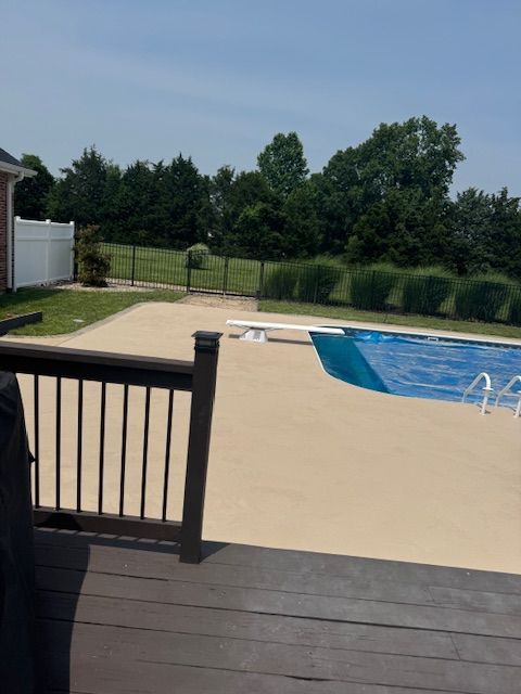 Backyard pool with a tan concrete deck, blue pool cover, and a black fence in the distance.
