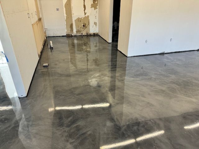 Shiny gray epoxy floor reflecting light in a room under construction, with white walls and exposed plaster.