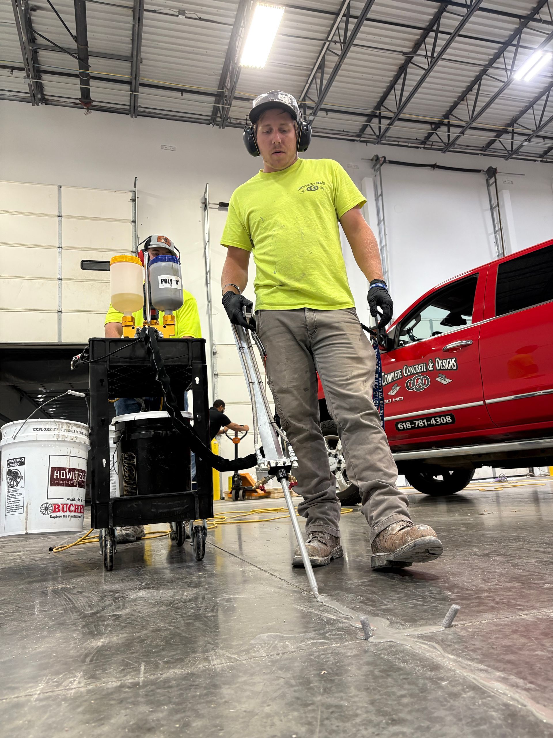 Man in a neon shirt and work boots using a concrete crack saw indoors, near a red truck and equipment.