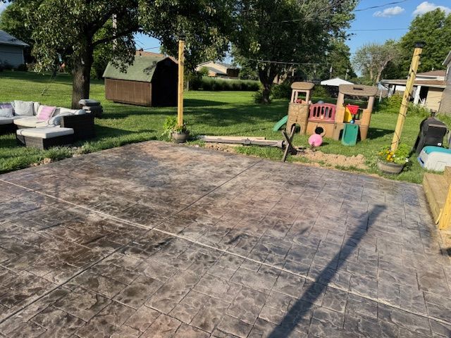 Stamped concrete patio with outdoor seating, playhouse, and yard in background.