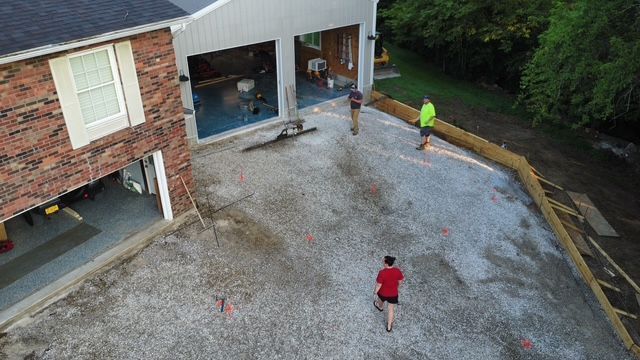 Construction site: Gravel driveway with workers near a building with garage bays, one person walking.