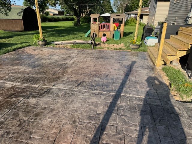 Stamped concrete patio in a backyard with a playhouse and wooden stairs.