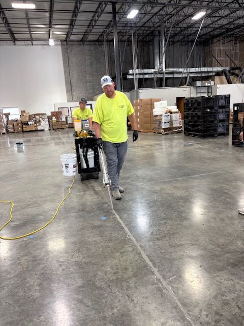 Two workers filling a crack in a concrete warehouse floor with a sealant machine.