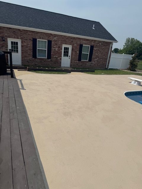 Backyard patio with a pool and a brick house. The patio is light-colored concrete.